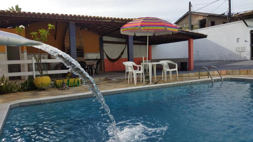 uma piscina com um guarda-sol, uma mesa e cadeiras em Diversão, churrasco e piscina - Praia de Ipitanga em Salvador