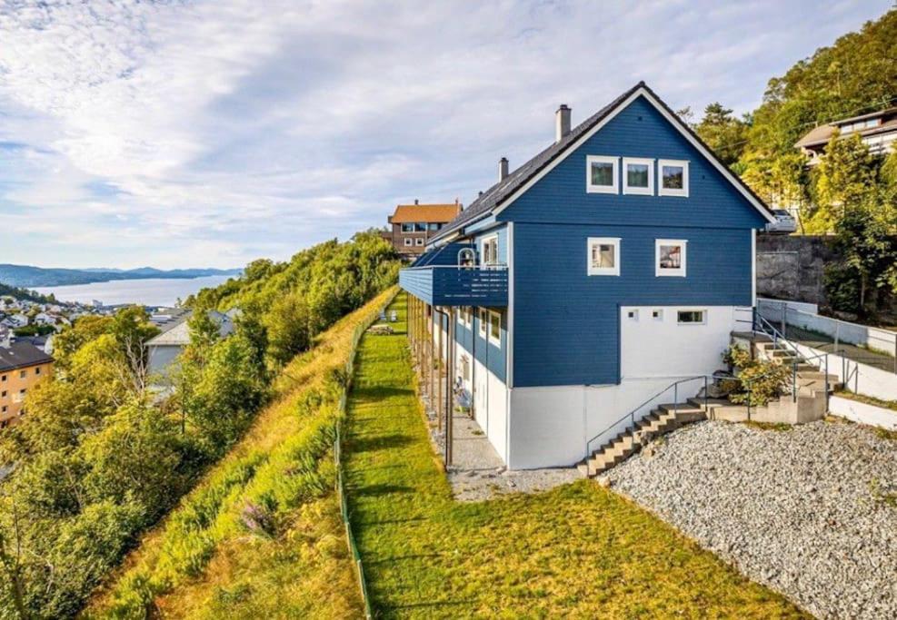 Cosy house with sunny terrace, garden and fjord view في بيرغِن: منزل أزرق على جانب تلة