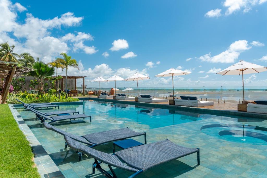 uma piscina com cadeiras e guarda-sóis em Villa Pantai Boutique Hotel Maragogi em Maragogi
