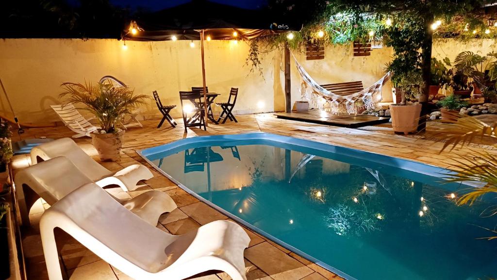 una piscina con 2 sillas blancas y una mesa en Brotas Suítes Belo Quinto & Spazzio Bloco 2, en Brotas
