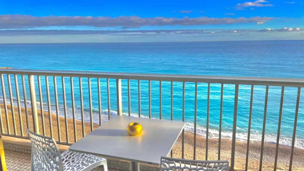 una mesa blanca y sillas en un balcón con vistas al océano en « LA SUITE »Superbe appartement NEUF, Front de mer, en Menton