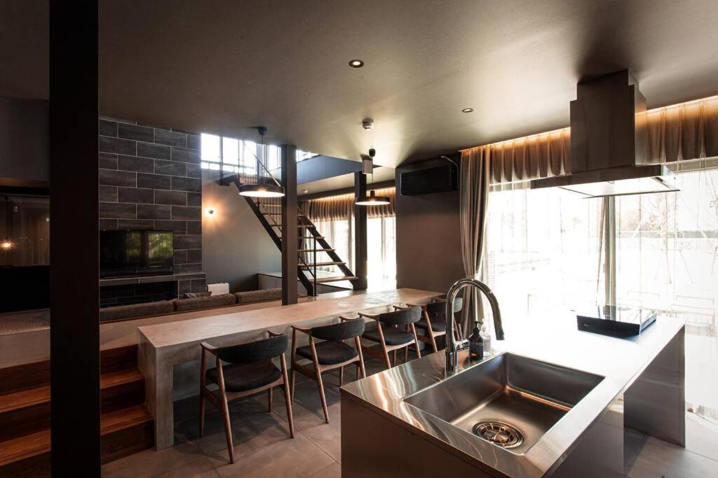 eine Küche mit einer Spüle und einer Theke mit Stühlen in der Unterkunft Itoshima 810 Villa & Resort in Keya