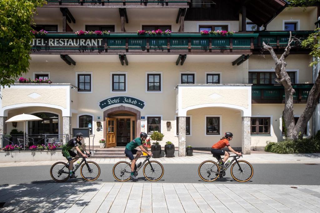 three people riding bikes down a street in front of a building at Rennrad- & Triathlonhotel Jakob in Fuschl am See