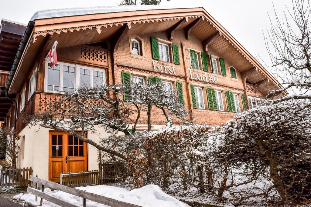 duży budynek z zielonymi okiennicami w śniegu w obiekcie First Lodge w mieście Grindelwald