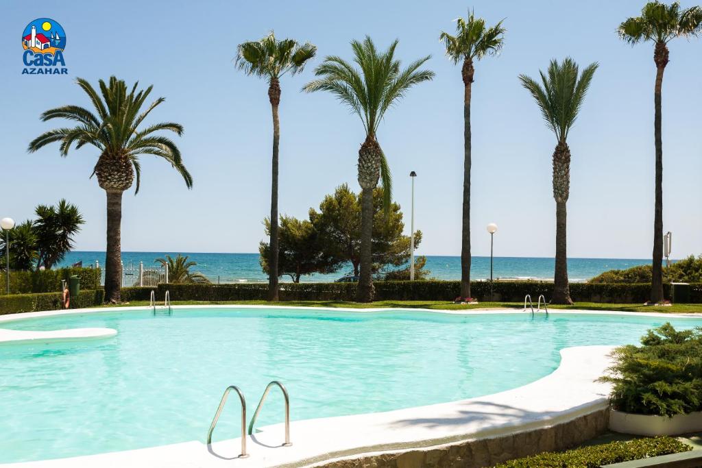 une grande piscine avec des palmiers et l'océan dans l'établissement Residencial Casablanca Casa Azahar, à Alcossebre