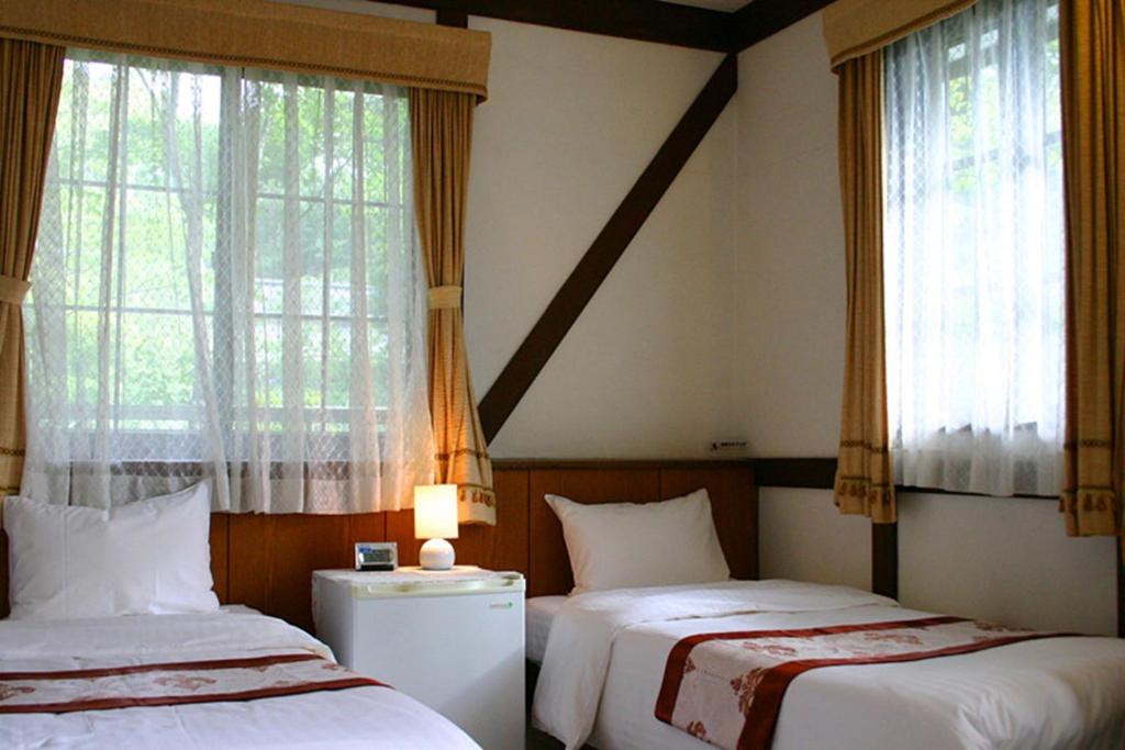 une chambre d'hôtel avec deux lits et des fenêtres dans l'établissement Pension Marieペンションマリエ, à Yamanakako