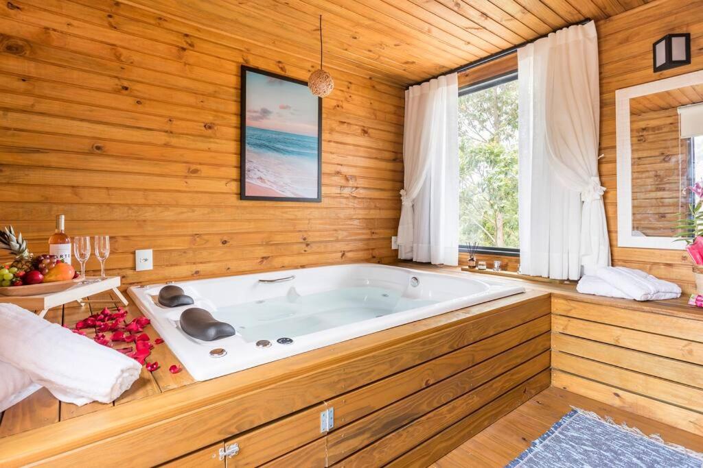 Casa com Banheira, Piscina e Quadra de Areia في إيمبيتوبا: حوض استحمام كبير في غرفة مع جدران خشبية