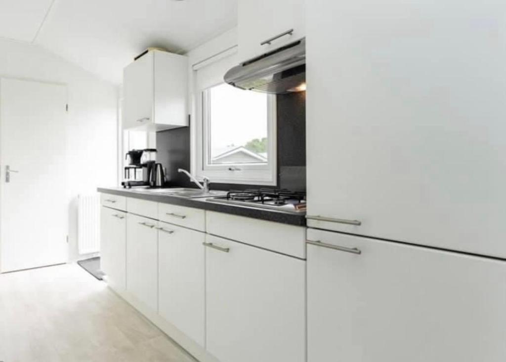 a white kitchen with white cabinets and a window at Ibiza huisje in Den Hoorn
