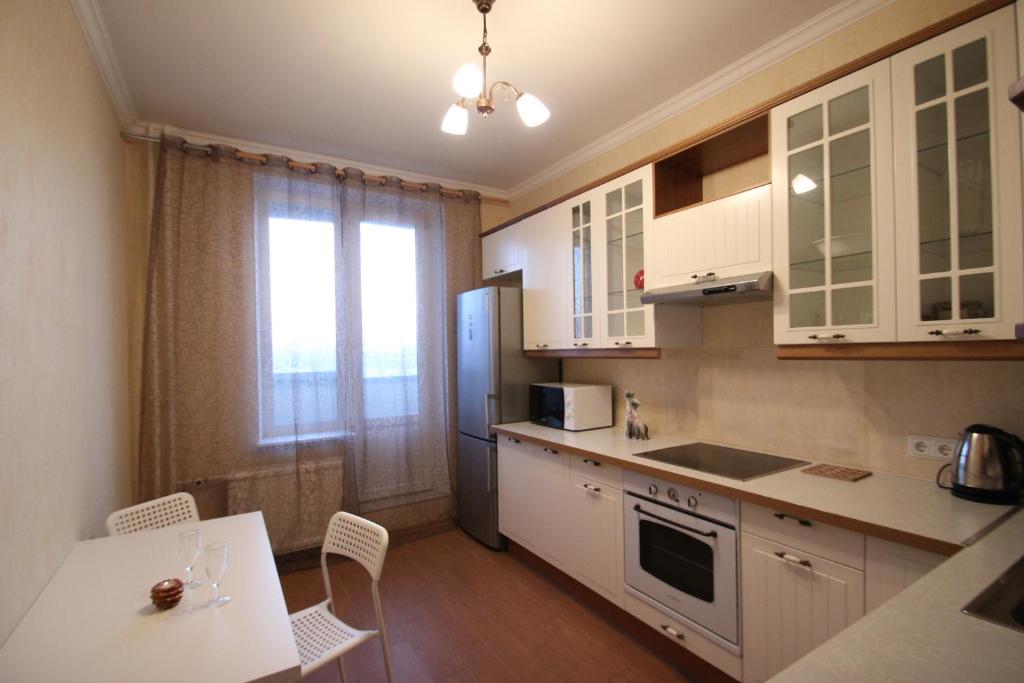 cocina con armarios blancos, mesa y nevera en Apartment u Yuzhnogo Polyusa, en San Petersburgo