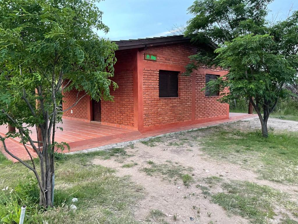 a red brick house with a deck in a yard at Cabañas Puerta del Sol - San Marcos Sierras in San Marcos Sierras