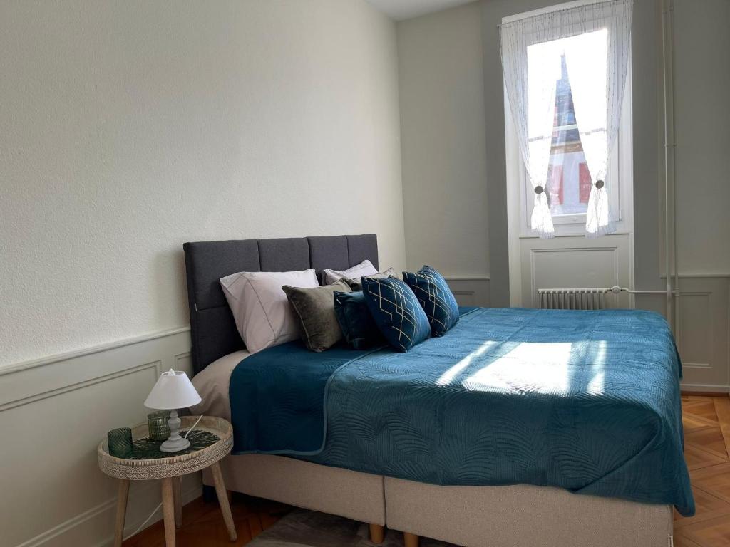 Schlafzimmer mit einem Bett mit blauer Bettwäsche und einem Fenster in der Unterkunft V&V CENTRE Neuchatel in Neuenburg