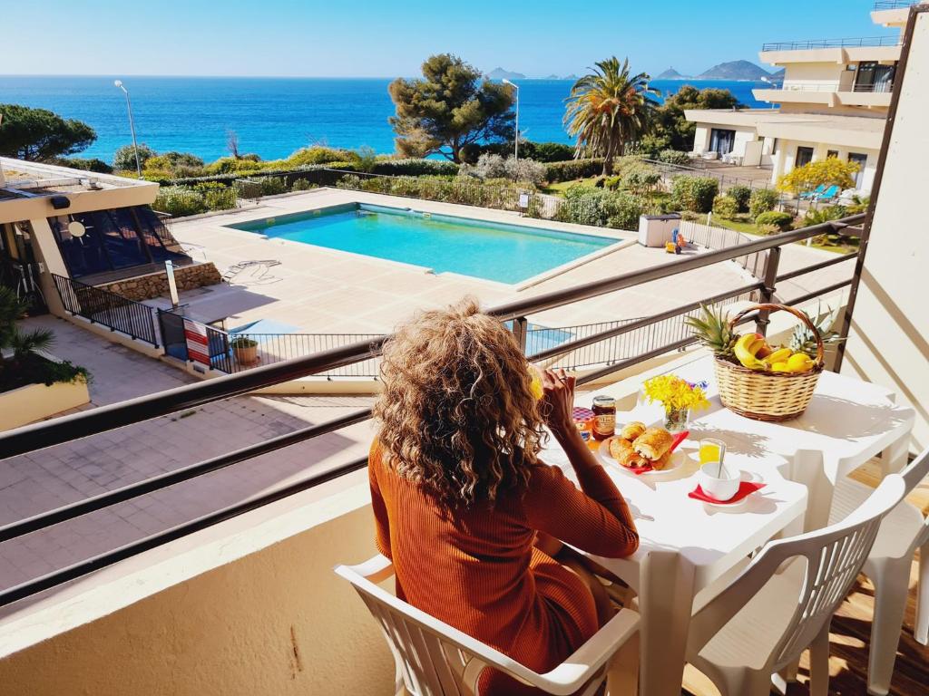 a woman sitting at a table on a balcony looking at the ocean at CosySeaside Corsica Ajaccio Piscine Terrasse Mer in Ajaccio