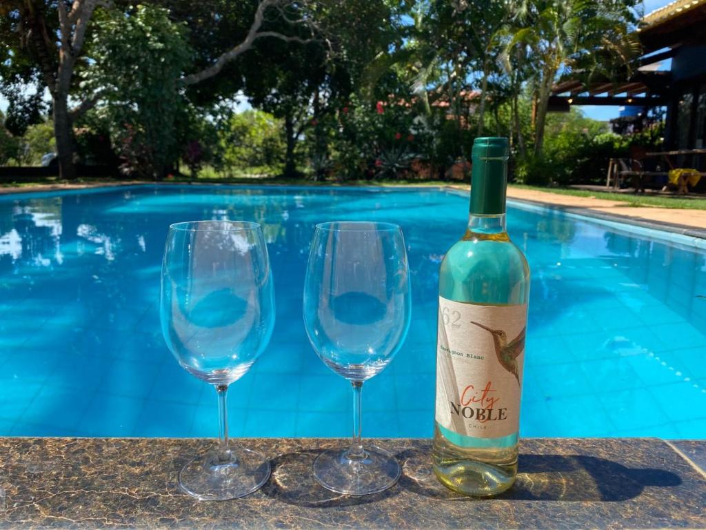 a bottle of wine and two wine glasses next to a swimming pool at Chalé com Piscina em Guaratiba- Prado in Prado