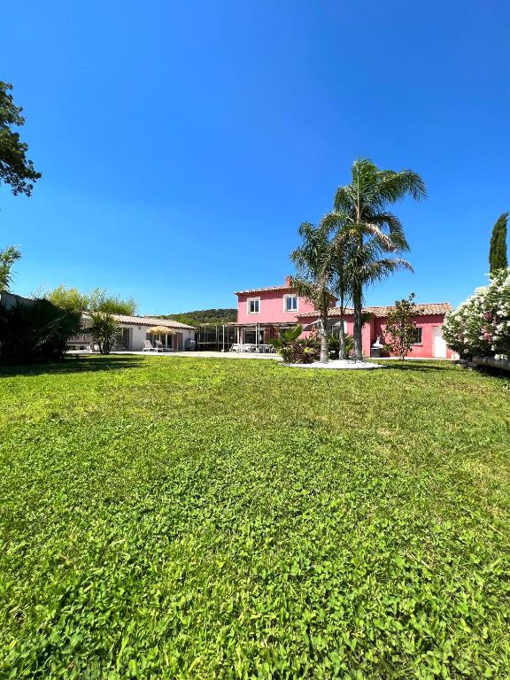 un grand champ herbeux avec un bâtiment rose et des palmiers dans l'établissement VILLA NOAVA, à La Crau