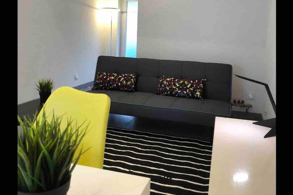 uma sala de estar com um sofá preto e uma cadeira amarela em Le Megève em Sainte-Croix-en-Plaine