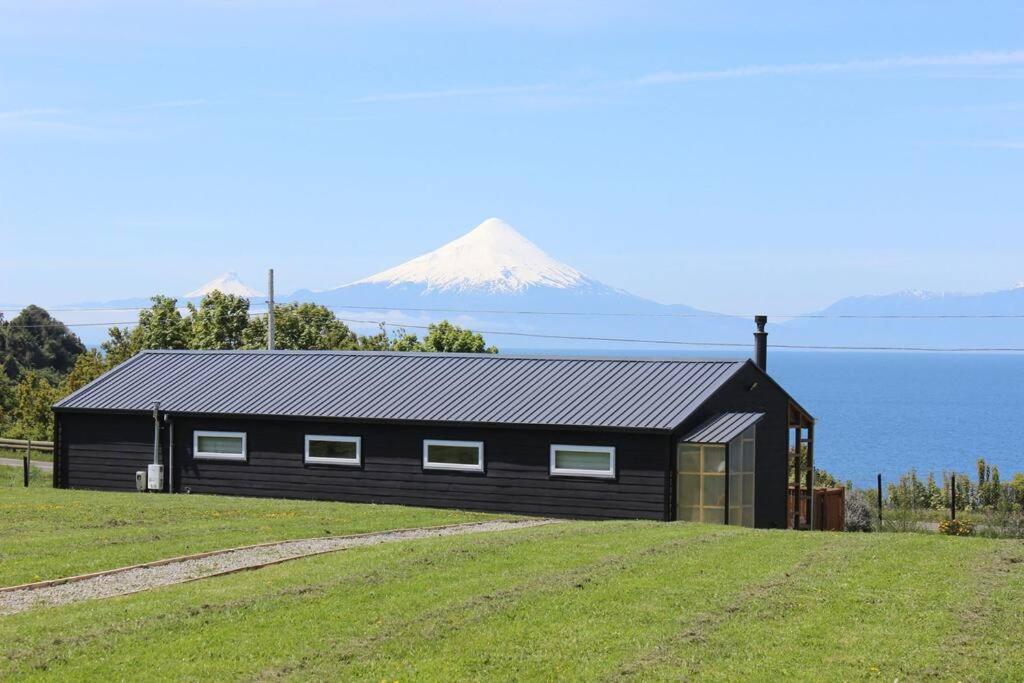 a black house on a hill with a mountain in the background at Cabaña frente al Lago Llanquihue in Llanquihue