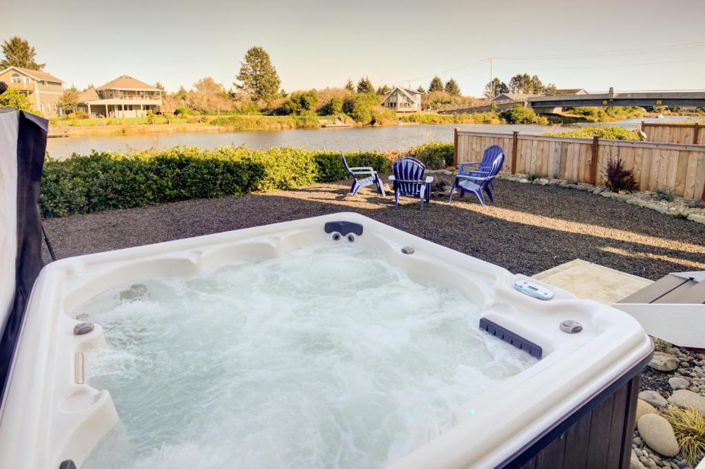 a hot tub in a yard with chairs and a lake at Gone Coastal Oyhut Bay Seaside Village in Ocean Shores