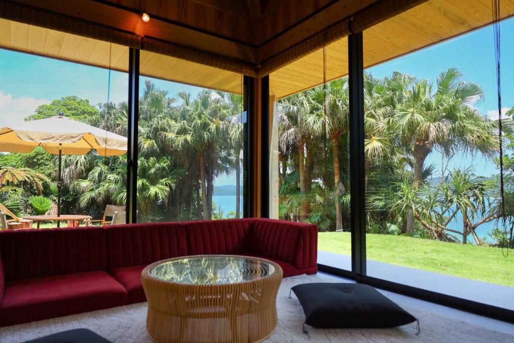 uma sala de estar com um sofá vermelho e janelas grandes em 泊まれるアートミュージアム 琉球ヴィラ em Tatsugo