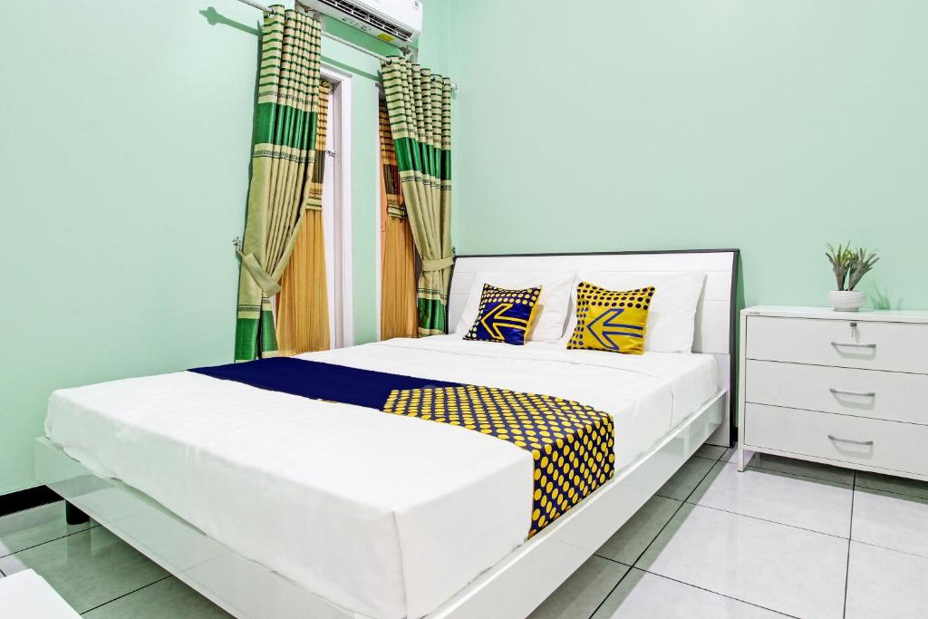 Un dormitorio con una cama blanca con almohadas amarillas y azules en SPOT ON 92012 Homestay Grand Mahkota Permai Syariah, en Cilacap