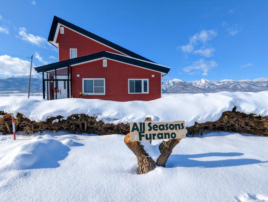 Un cartello nella neve davanti a una casa rossa di All Seasons Furano Chalet a Furano