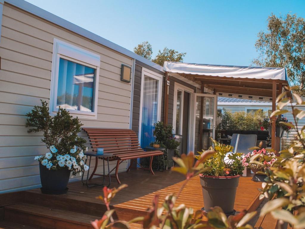 una casa con una terraza con macetas y un banco en Camping Les Jardins de la Mer en Merlimont