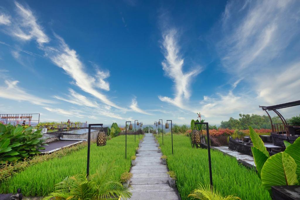 a pathway through a field of grass with a blue sky at Abhayagiri - Sumberwatu Heritage Resort in Yogyakarta