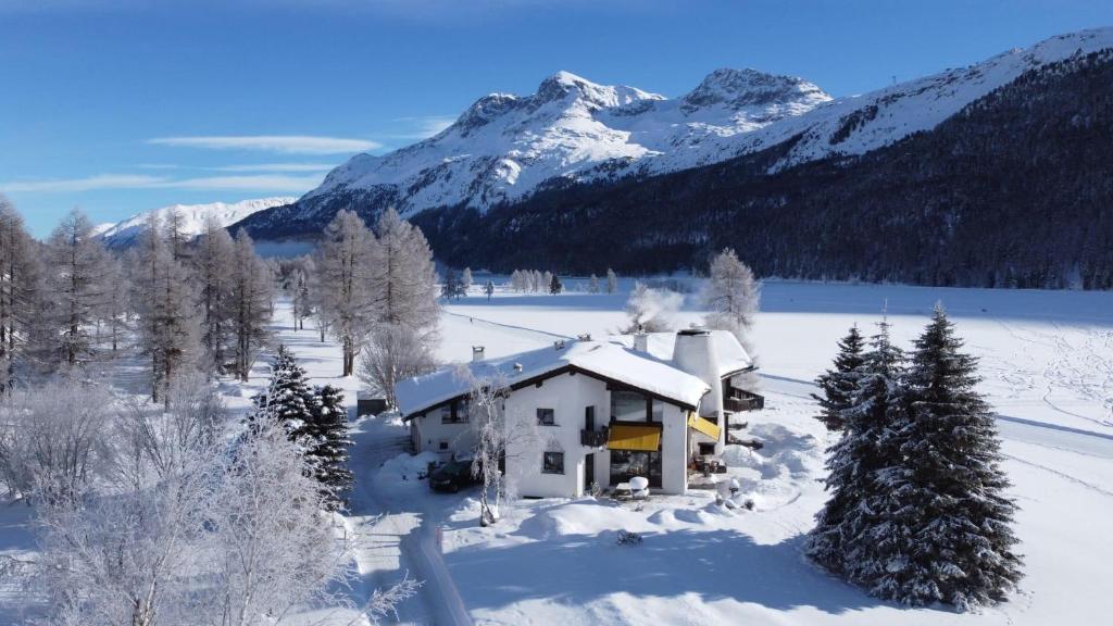 a house in the snow with mountains in the background at Chesa Suot Ovas in Sils Maria