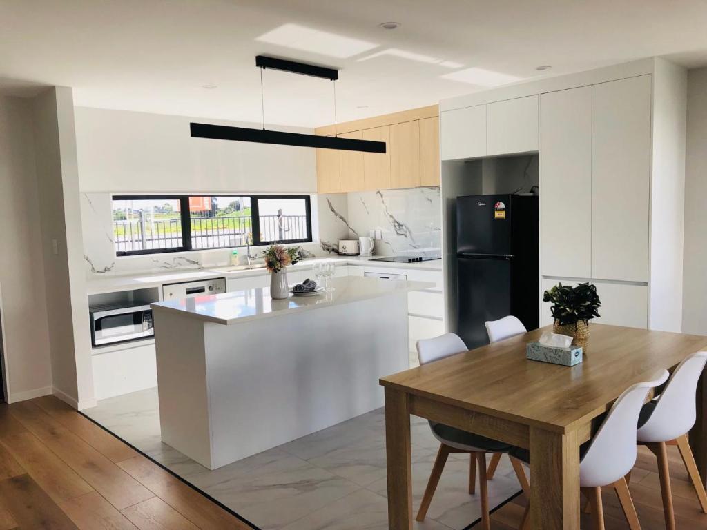 a white kitchen with a wooden table and a table and chairs at Modern & Luxurious Home 3 in Auckland