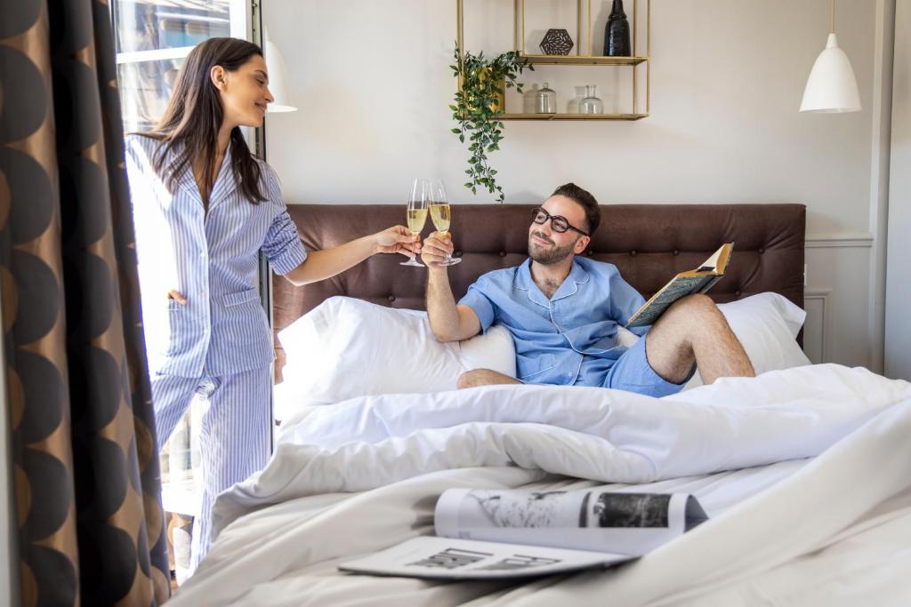 a woman giving a man a glass of wine in bed at Hôtel Madeleine Haussmann in Paris