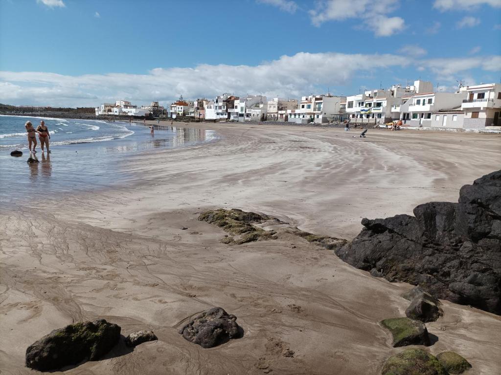 two people walking on a beach with rocks and houses at La casa de la playa in Las Palmas de Gran Canaria