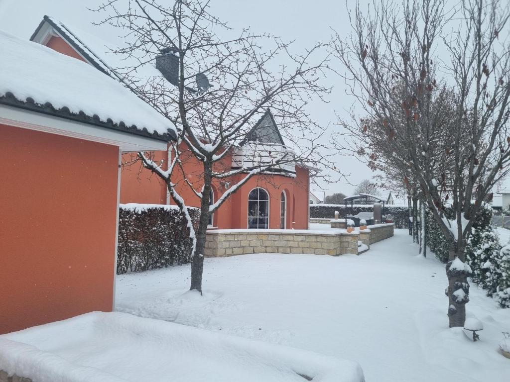 a snow covered yard with a red house and trees at Ferienwohnung am Stadtrand von Dresden in Kesselsdorf