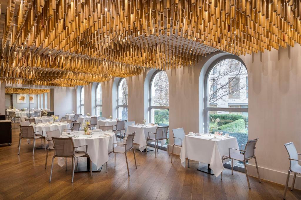 a dining room with white tables and chairs and chandeliers at COMO The Halkin in London