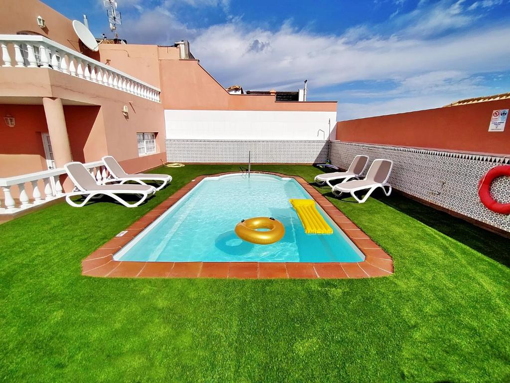 a small swimming pool on a lawn with two chairs at Vv ORAMAS in Caleta De Fuste