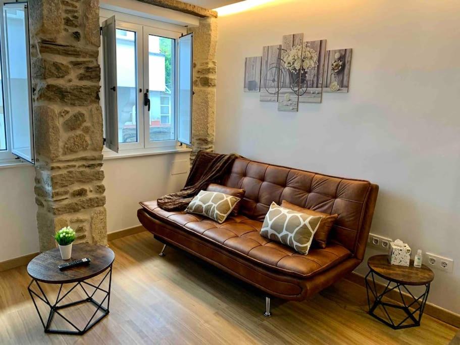 ein braunes Ledersofa in einem Wohnzimmer mit zwei Tischen in der Unterkunft Bonito apartamento en el centro de Pontedeume. in Puentedeume