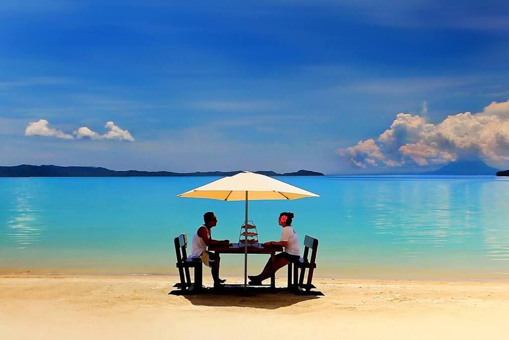 a couple sitting at a table under an umbrella on the beach at Gilligans Port Barton Beach Resort in San Vicente