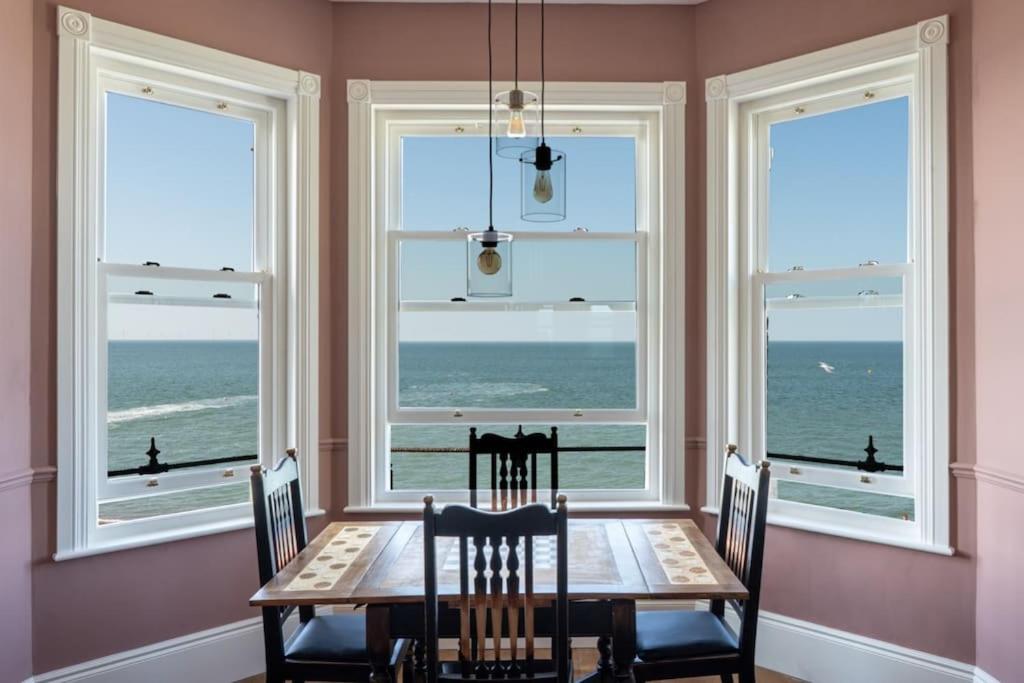 a dining room with a table and four windows at Stylish Beachfront Apartment, Sweeping Ocean Views and Luxury Touches in Herne Bay