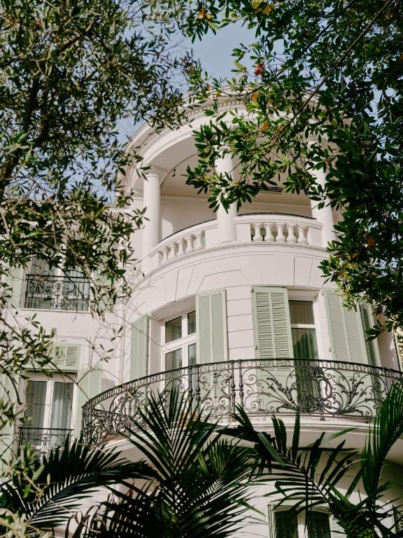 a white building with a balcony and trees at Hôtel & Spa Belle Plage in Cannes