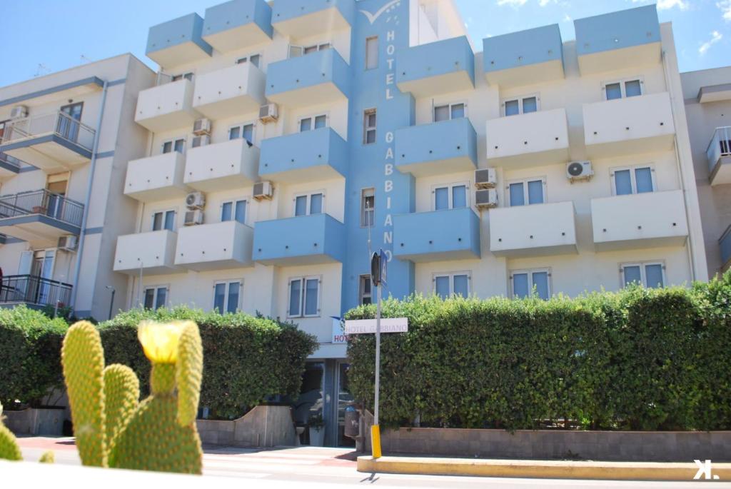 un grand bâtiment avec un cactus en face dans l'établissement Hotel Gabbiano, à Mola di Bari