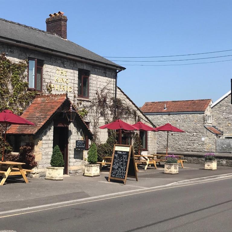 um restaurante com mesas e guarda-sóis em frente a um edifício em The King Alfred em Street