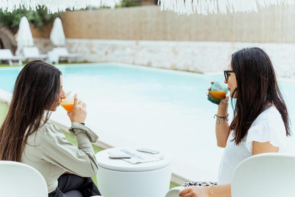 two women drinking orange juice in front of a pool at Tuo Hotel in Polignano a Mare