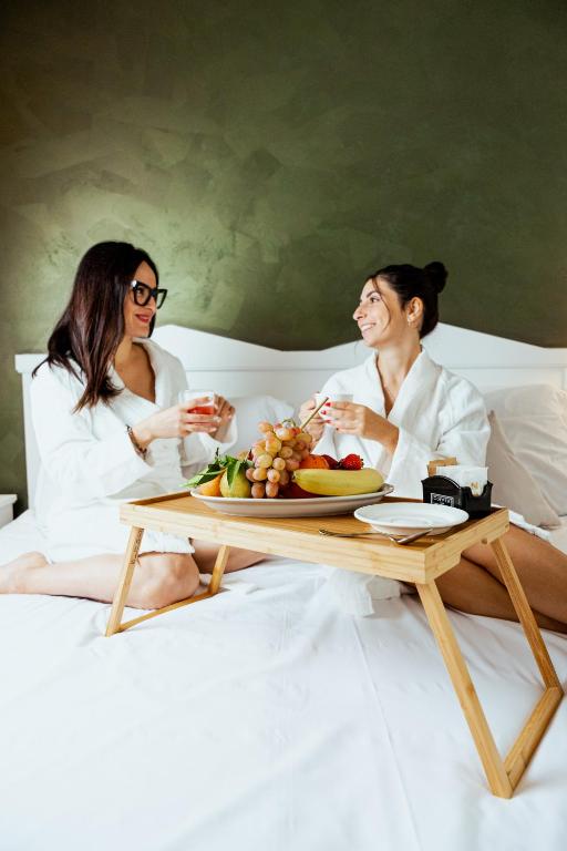 two women sitting on a bed with a table with a plate of food at Tuo Hotel in Polignano a Mare