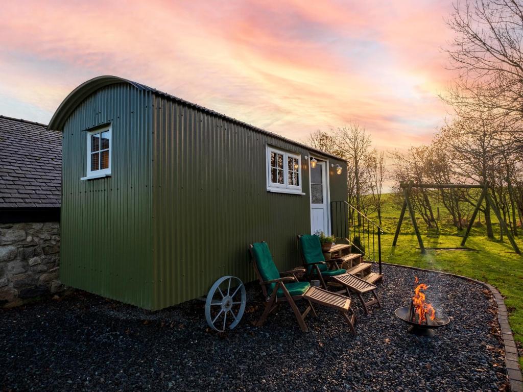ein grünes Gebäude mit Stühlen und einem Kamin davor in der Unterkunft The Pleasant Hut at MountPleasant Farm in Ulverston