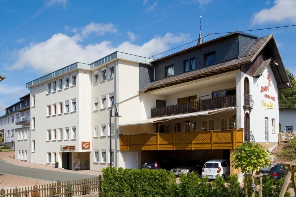 a white building with a yellow balcony at Merker's Hotel & Restaurant Bostalsee in Bosen-Eckelhausen