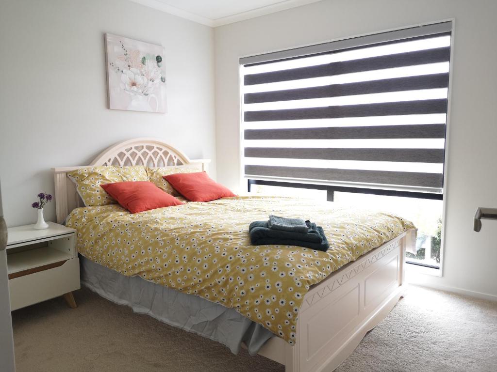 a bedroom with a bed with red pillows and a window at Orewa Lovely Cozy Home in Auckland