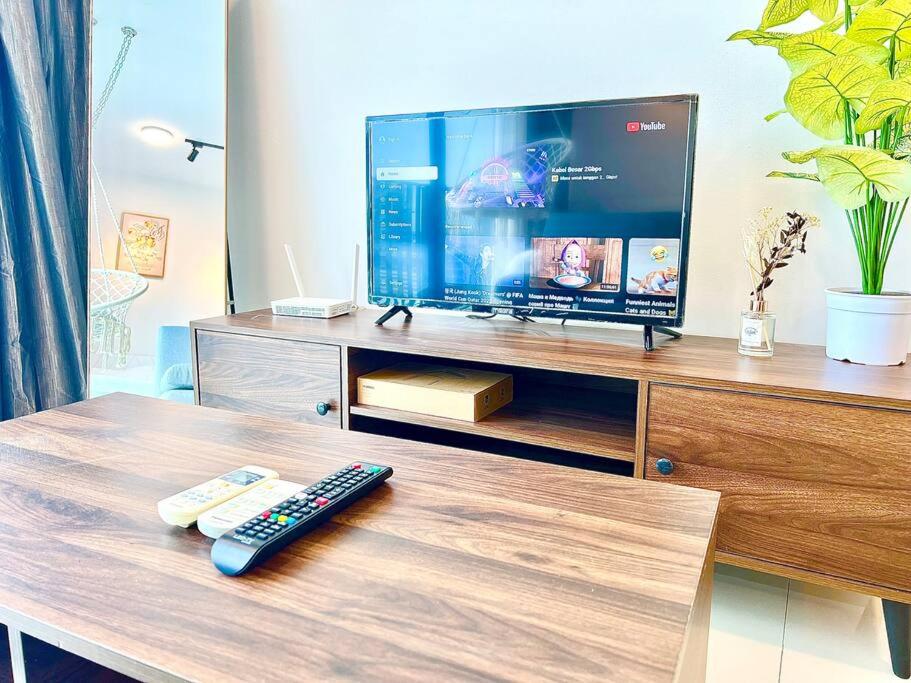 a tv on a wooden stand with a remote control at G 1-5pax Cozy Home Trefoil Setia Alam 100mps Wifi & TV SCCC in Setia Alam