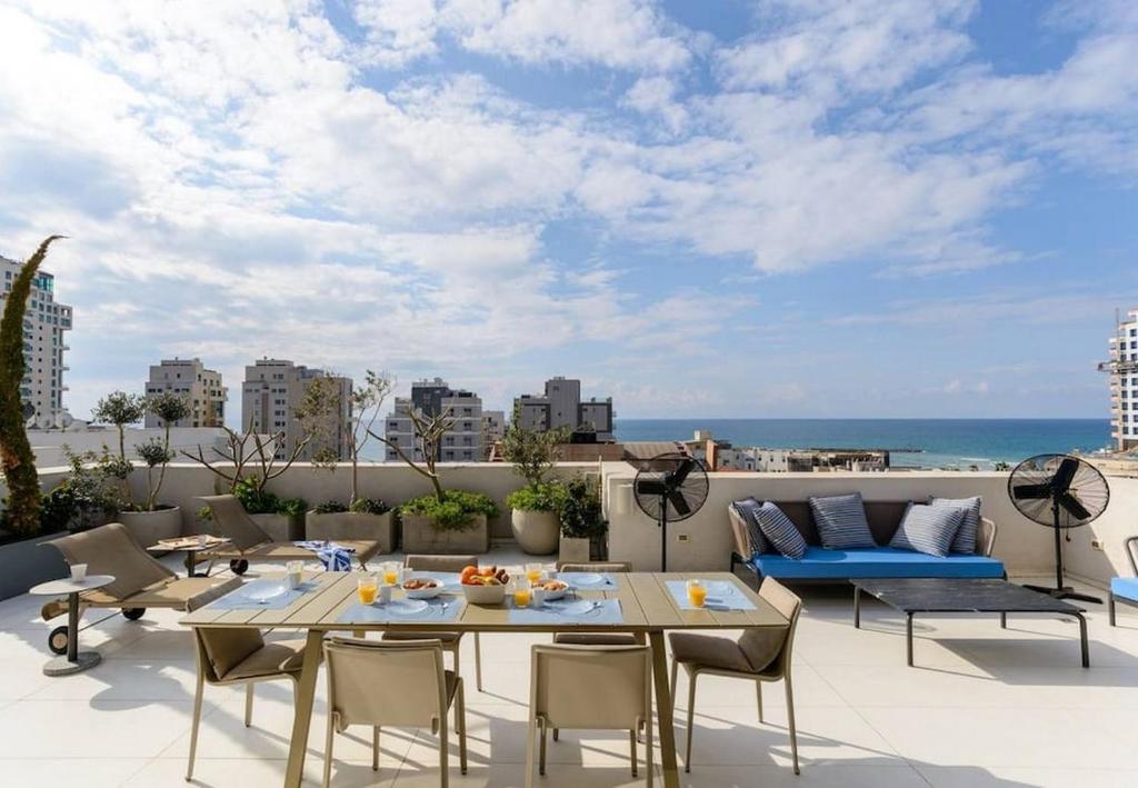 eine Terrasse mit einem Tisch, Stühlen und Meerblick in der Unterkunft Spacious 5BR Penthouse Sea views by Holyguest in Tel Aviv