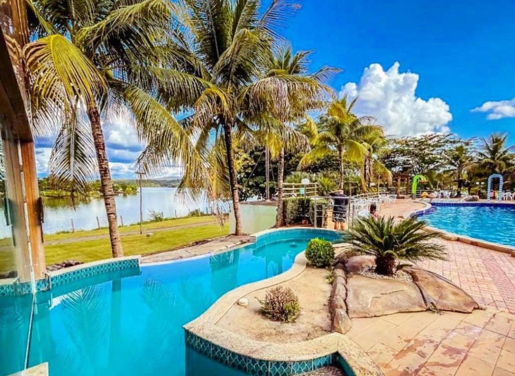 a resort pool with palm trees and a body of water at Flat no Pontal do Lago in Caldas Novas