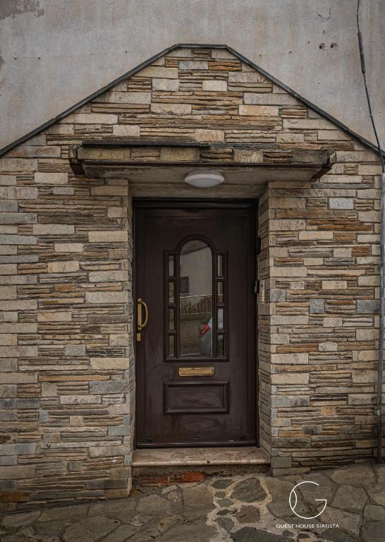 a brick building with a black door with a window at Guest House Siatista in Siátista