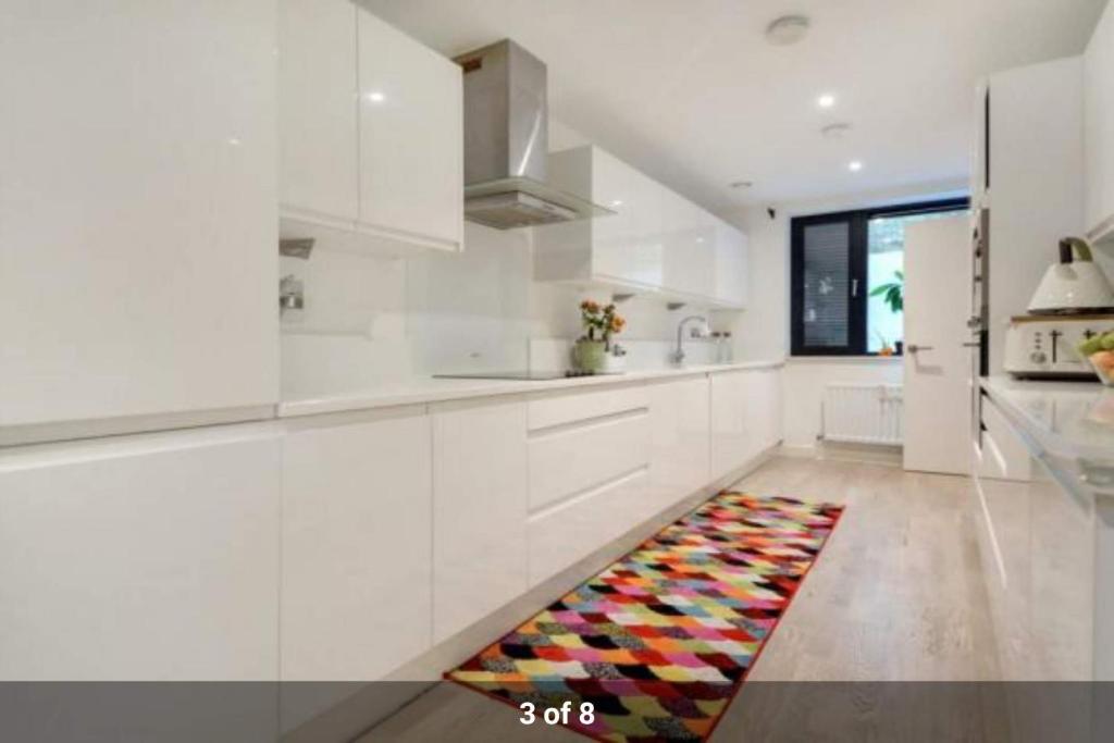 a kitchen with white cabinets and a rug on the floor at London Holiday Home - Entire 4 Bedroom Private House with Kitchen, Living Room & private Garden - 1 Cape House London, Within 30 mins from Central London, London Bridge & Canary wharf in London
