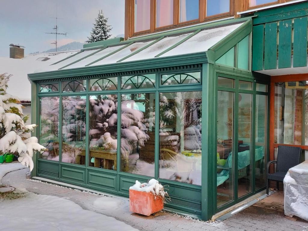 ein mit Schnee bedecktes Gewächshaus vor einem Haus in der Unterkunft Konstanzer Bergblick mit Wintergarten in Oberstaufen
